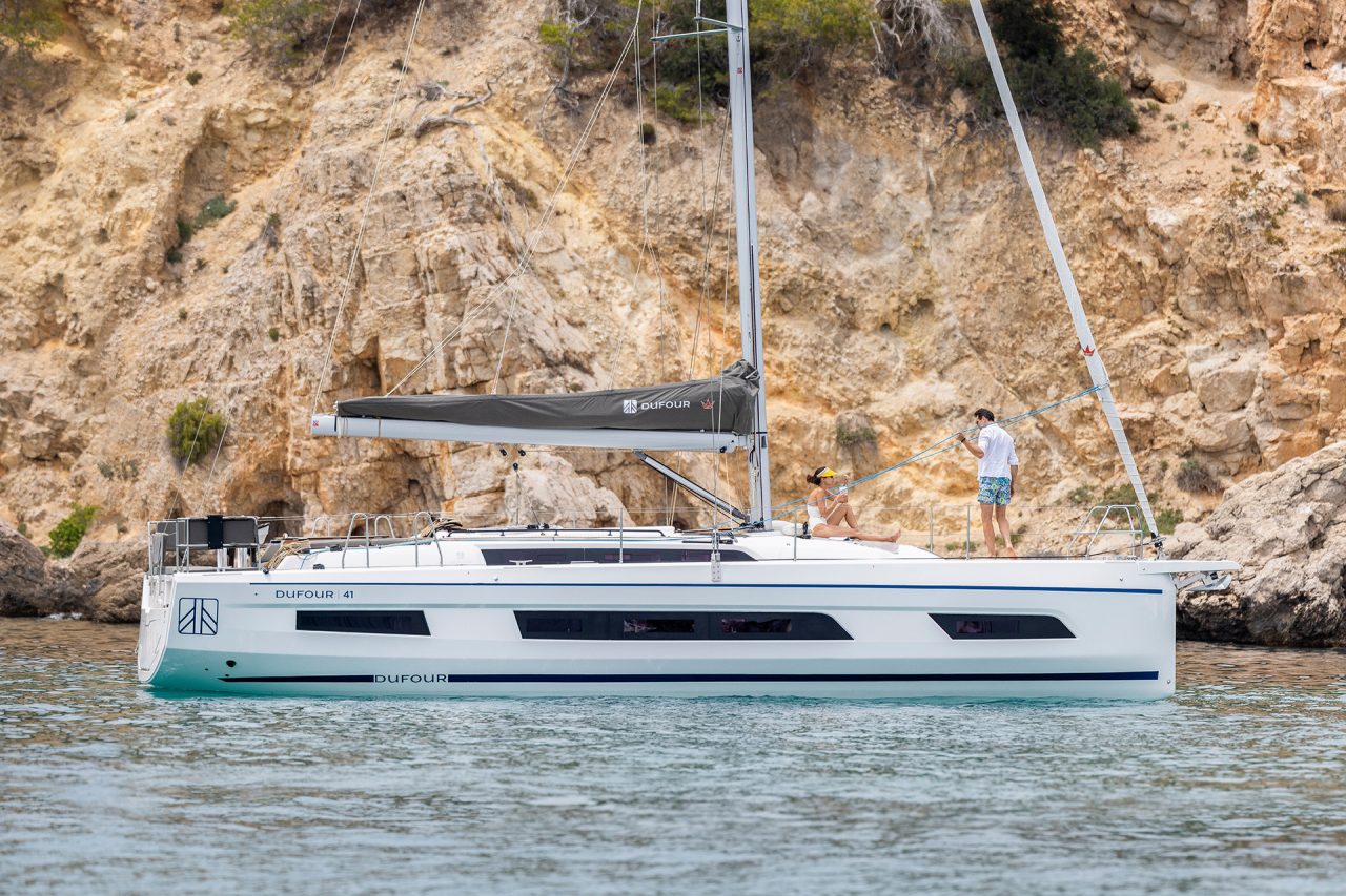 Side view of the Dufour 41 sailing boat at anchor with rugged cliff backdrop