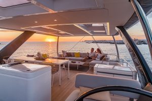 Couple lounging on Lagoon 77 luxury catamaran flybridge at sunset